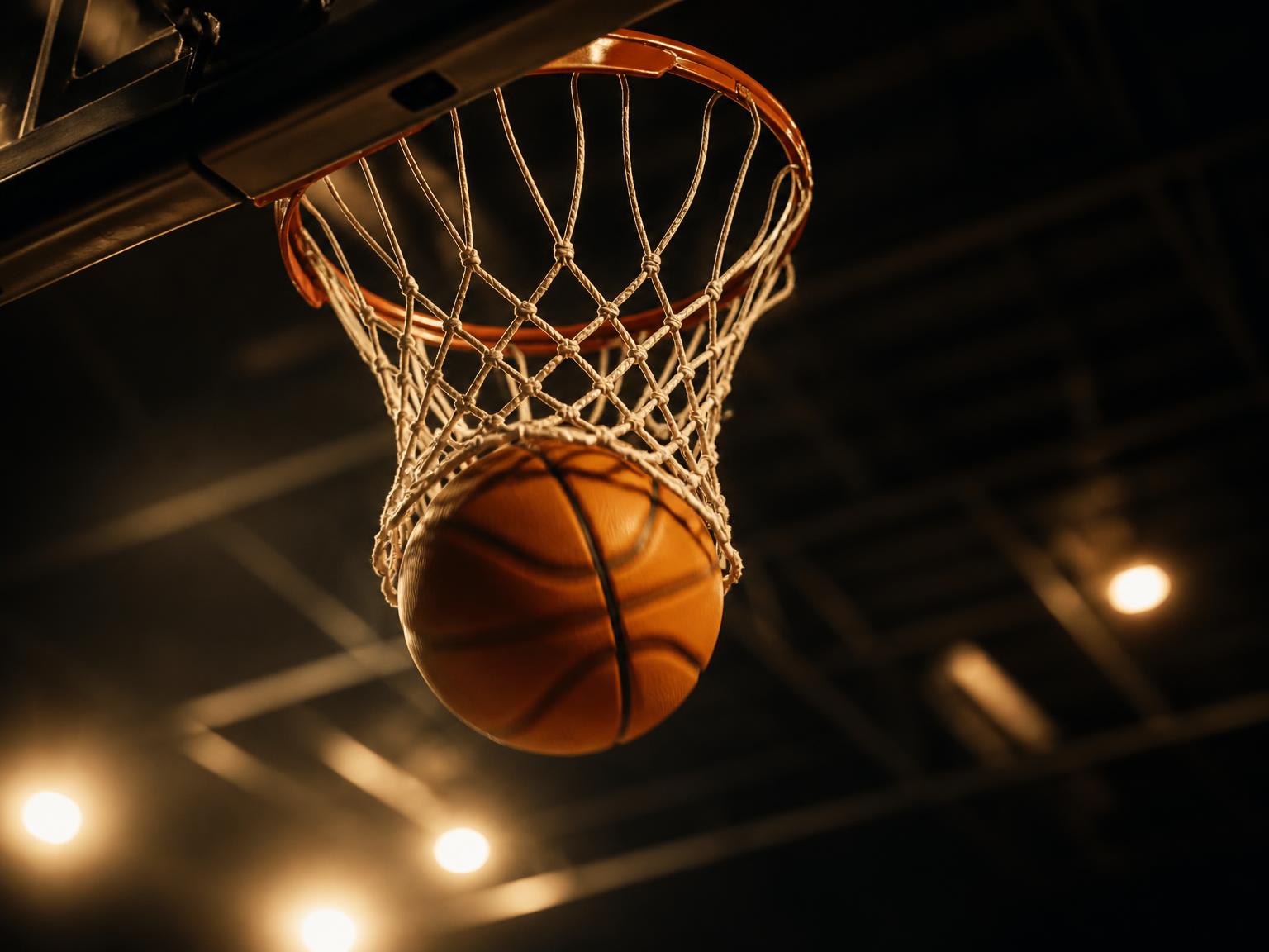 Basketball dropping through the hoop in a dark gym, lit in gold